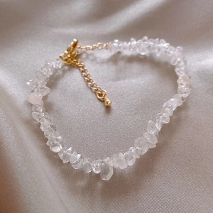 Detailed close-up of irregular clear crystal bracelet with gold clasp and silk background