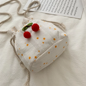 White canvas bucket bag with yellow daisy embroidery and red cherry pendant detail