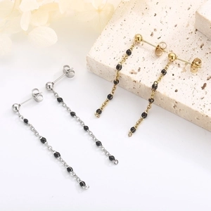 Detail of gold and silver tassel chain earrings with black resin beads on white stone