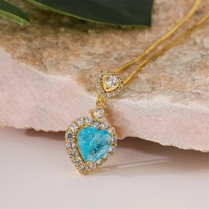 Close-up of gold necklace with blue heart crystal pendant on natural stone background