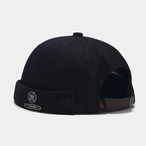 Detail of black docker cap with a metal leaf emblem and adjustable leather strap