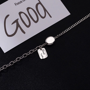 Silver chain necklace with Good Luck rectangular tag and round bead on dark background