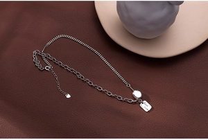 Detail of silver double-layered chain necklace with Good Luck engraved square pendant
