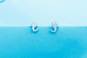 Detail of silver scorpion-shaped stainless steel stud earrings on a blue background