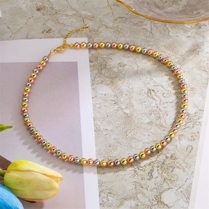 Detailed view of tri-color metal bead necklace with lobster clasp on marble surface
