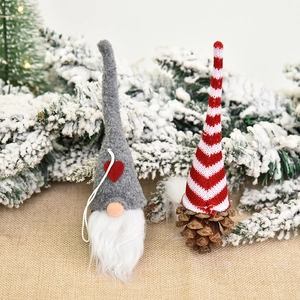Christmas gnome ornaments with grey felt and red striped hats on snowy pine branches