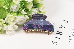 Close-up of acetic acid hair claw with purple and blue floral patterns on a white book