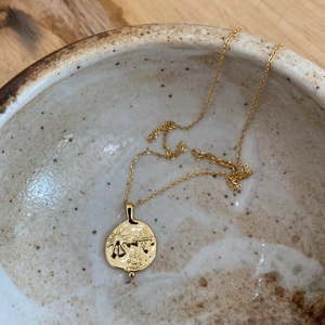 Macro detail of a 925 silver sun coin pendant resting inside a rustic ceramic bowl