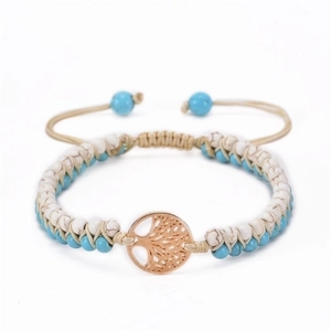 Detail of hand-woven turquoise and white stone bracelet with gold tree of life charm
