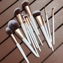 Detail of 12-piece makeup brush set with white handles and gold ferrules on dark wood
