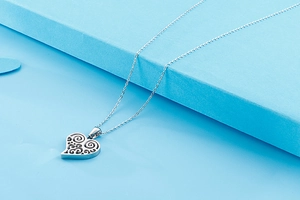 Gros plan du pendentif cœur évidé en argent sur une fine chaîne et fond géométrique