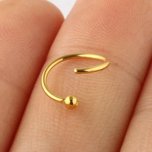 Macro shot of a polished 18K gold-plated nose ring with a ball end on a finger joint