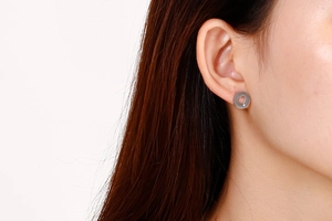 Close-up of silver steel stud earrings with heart cutout and zircon worn by a model