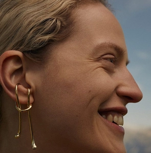 Close-up of elegant gold plated irregular cuff earring on woman's ear against sky