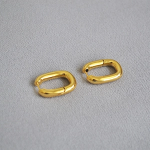 Détail des boucles d'oreilles créoles dorées en forme de U sur tissu texturé