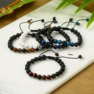 Tiger eye and lava stone beaded bracelets on white marble with natural green leaves