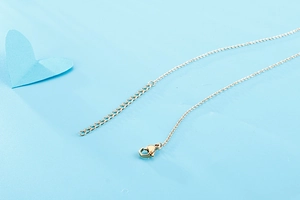 Detail of gold necklace with lobster clasp and extension chain on light blue surface