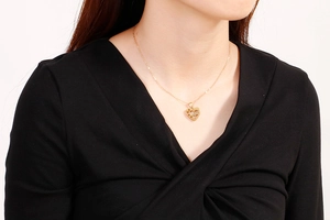 Collier doré en forme de cœur avec gravure 'love' porté par un mannequin sur un col en V noir