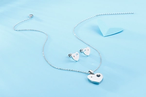 Close-up of silver hollow heart-shaped necklace and stud earrings set with crystal detail