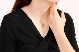 Close-up of a heart-shaped gold pendant necklace with diamond inlay on a female model