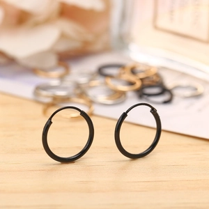 Macro shot of minimalist matte black hoop earrings on a warm wooden surface