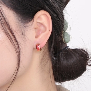 Close-up of rose gold huggie earring featuring a rectangular red gemstone on female model