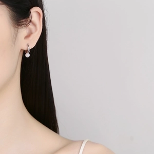 Elegant silver hoop earrings with white pearl pendant worn by model on grey background