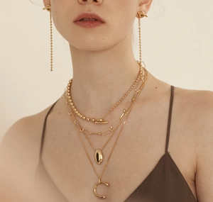 Detail of layered gold-plated necklaces with a letter C pendant and bead tassel earrings