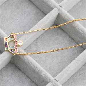 Close-up of golden crown pendant with colorful zircons on a box chain necklace