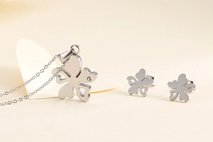 Détail de parure bijoux trèfle argenté avec collier et boucles d'oreilles sur beige