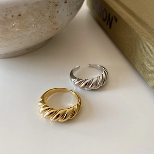 Detail of twisted croissant rings in gold and silver finish with wavy texture on table