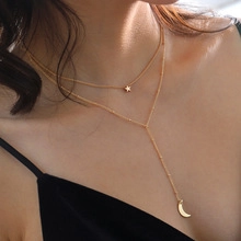 Model wearing a gold double-layer necklace featuring star and moon geometric pendants