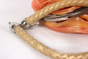 Detail of orange silk handbag featuring golden braided handle and silver metal clasp