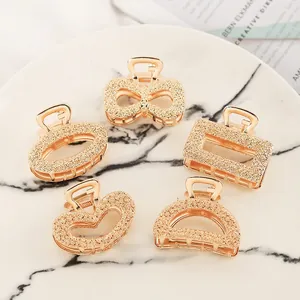 Five-piece set of gold geometric metal hair claws with glitter finish on marble tray