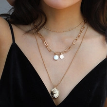 Macro view of layered gold necklace with pearl pendant and coin charm on a model