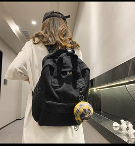 Detail of a black canvas backpack with a yellow plaid charm shown on a model