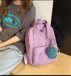 Pink canvas backpack with green plaid hat charm shown on model for back view detail