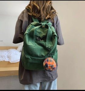 Rear view of a green canvas backpack with a plaid charm shown in a cozy home setting