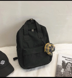 Detail of a black canvas backpack with adjustable straps and yellow plaid pendant