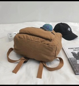Top-down view of brown canvas backpack with adjustable straps on a white fabric surface