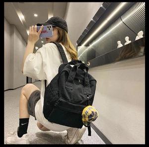 Detail view of a black canvas backpack featuring a yellow plaid pendant and simple design