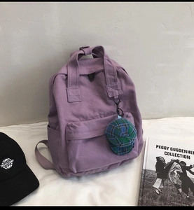 Detailed close-up of a purple canvas backpack with cute charm in a casual bedroom setting