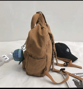 Side view of brown canvas backpack with a checkered charm and casual travel aesthetic