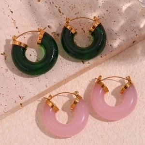 Detail of pink and green acrylic C-shape hoop earrings on a textured stone base