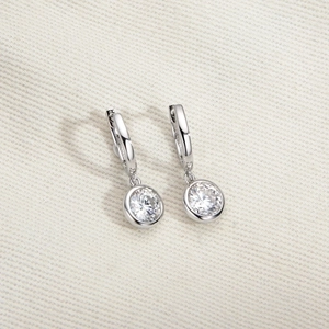 Macro shot of silver drop earrings featuring sparkling round stones on a white fabric texture