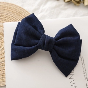 Detailed view of dark blue fabric bow hair clip on minimalist aesthetic background