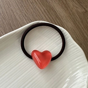 Detail view of a black elastic hair tie with a translucent red heart acrylic pendant