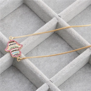Macro shot of gold Hamsa pendant with colorful zircon stones on gray velvet tray