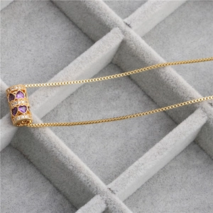 Détail macro du pendentif cylindre doré avec cœur en zircone violette sur velours gris