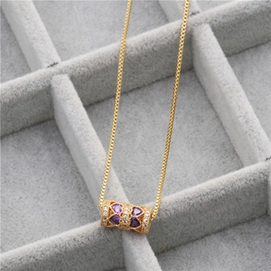 Détail du collier doré avec pierre cœur violette dans un plateau à bijoux gris